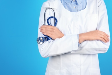 Female doctor holding stethoscope on color background, closeup