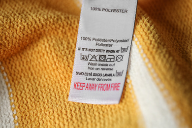 Photo of Clothing label with care symbols and material content on yellow shirt, closeup view
