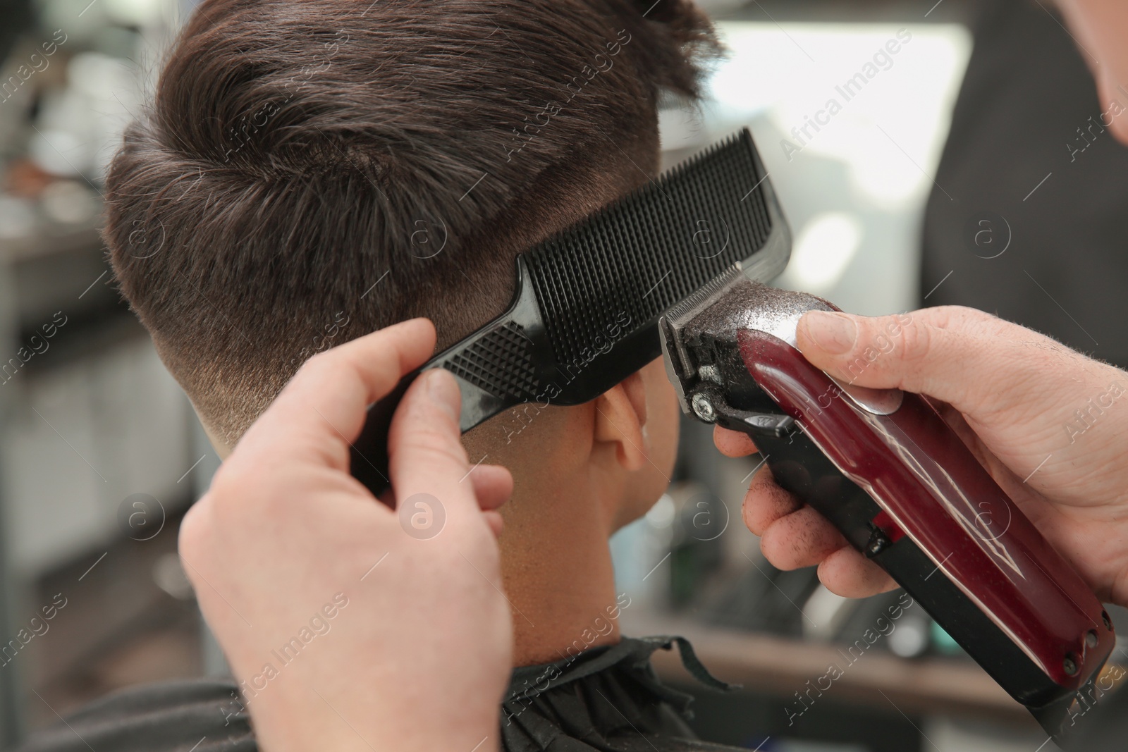 Photo of Professional barber making stylish haircut in salon, closeup