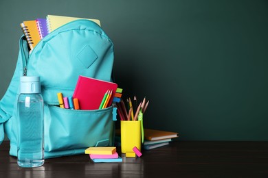 Backpack with different school stationery on wooden table near chalkboard, space for text