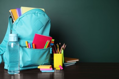 Photo of Backpack with different school stationery on wooden table near chalkboard, space for text