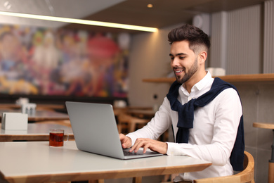 Photo of Young male business owner working with laptop in his cafe