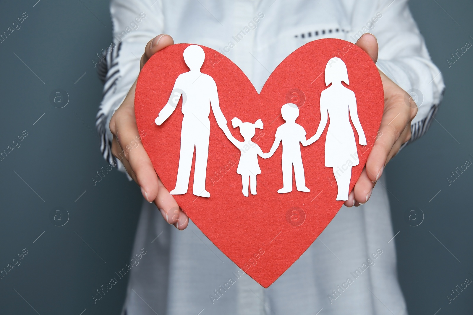 Photo of Woman holding red heart and paper family cutout, closeup