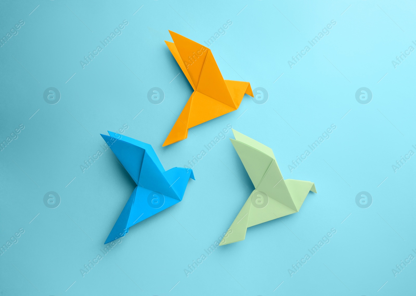 Photo of Origami art. Colorful handmade paper birds on light blue background, flat lay