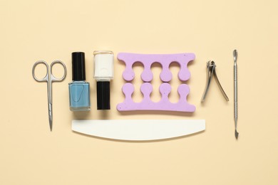 Nail polishes and set of pedicure tools on beige background, flat lay