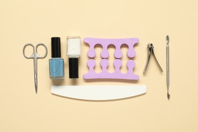 Photo of Nail polishes and set of pedicure tools on beige background, flat lay