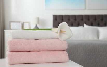 Photo of Stack of clean towels with flower on table in bedroom. Space for text