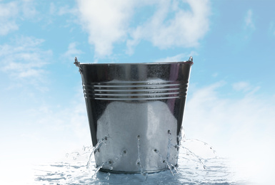 Image of Leaky bucket with water against blue sky 