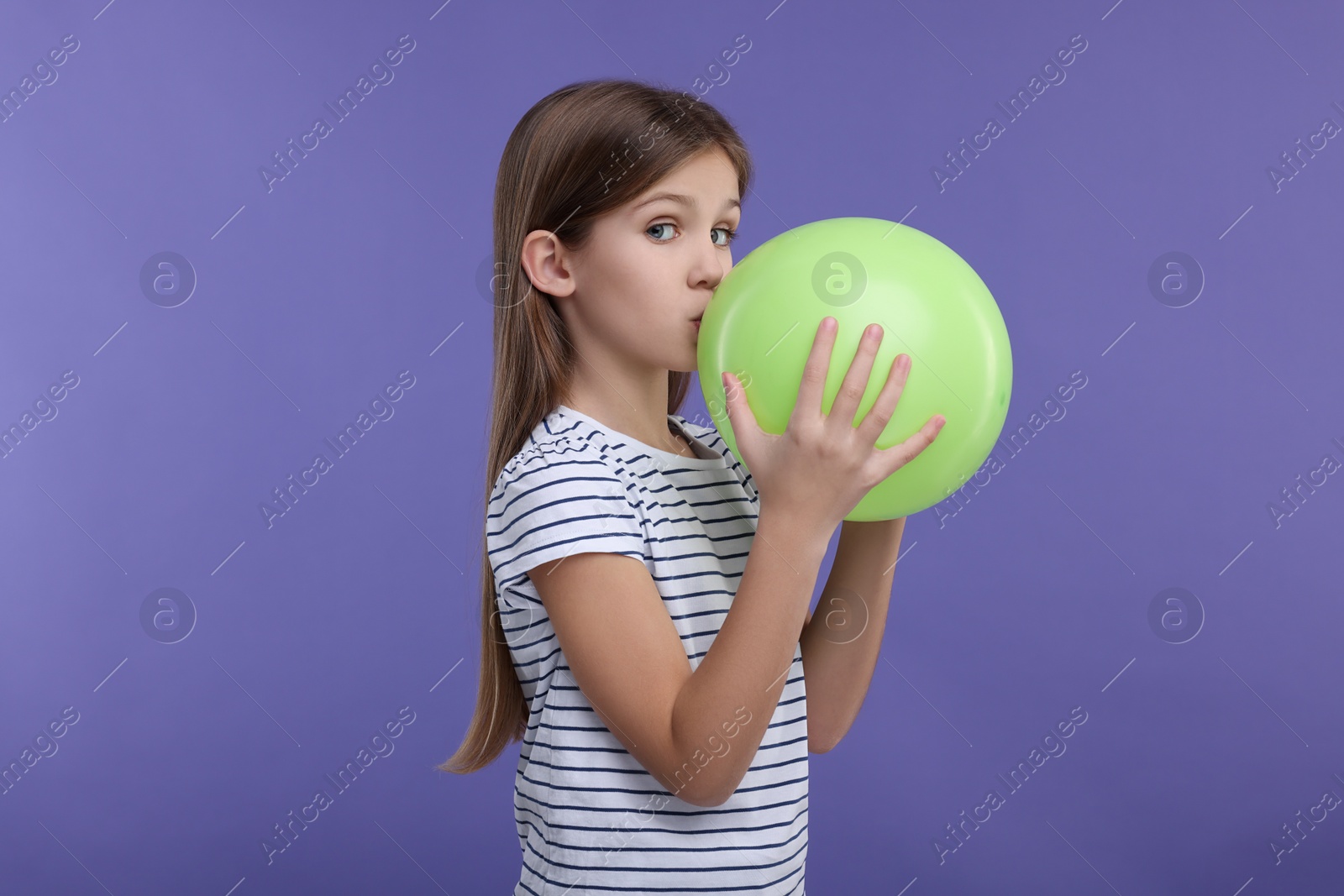 Photo of Girl inflating light green balloon on violet background