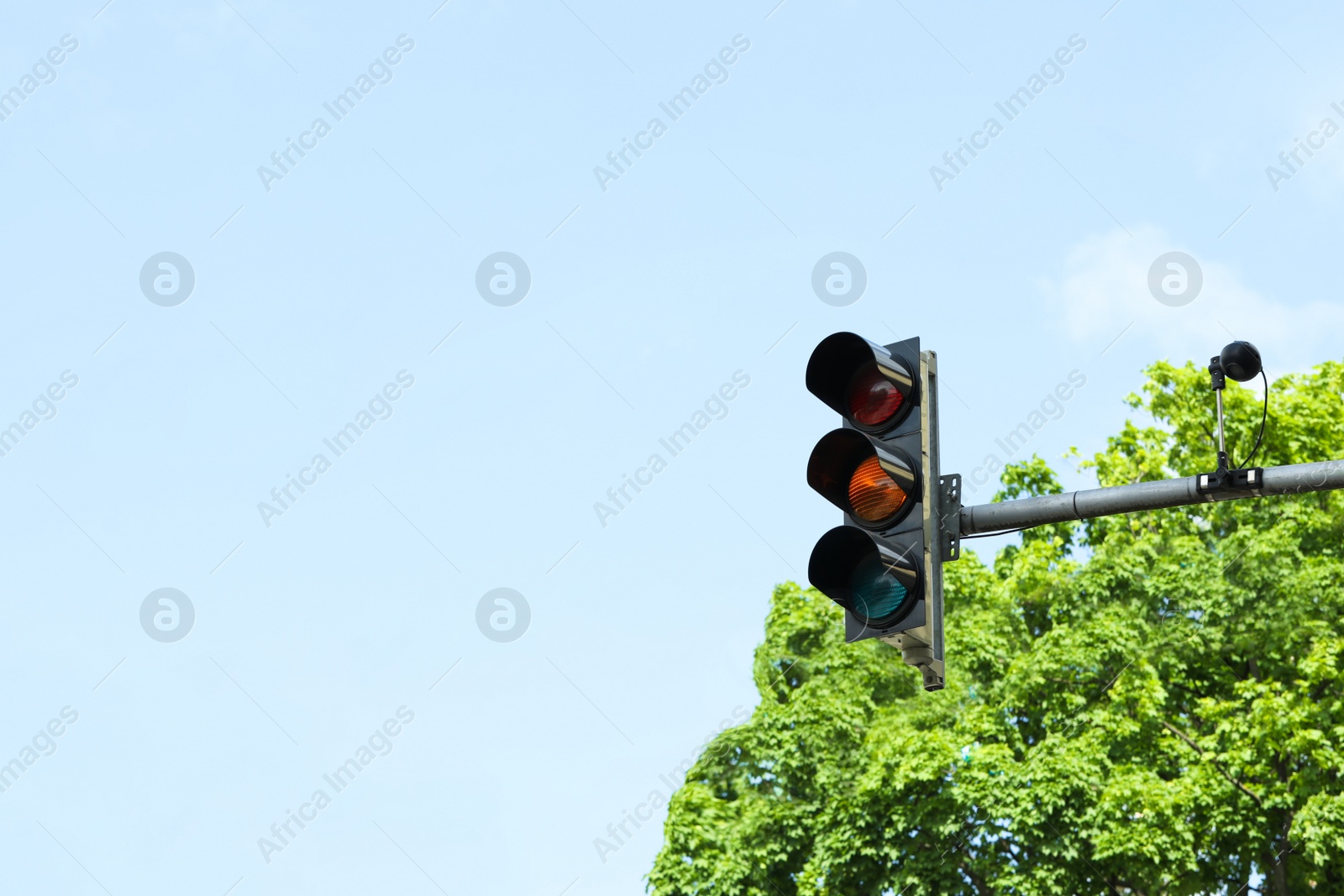 Photo of Traffic light near trees against cloudy sky