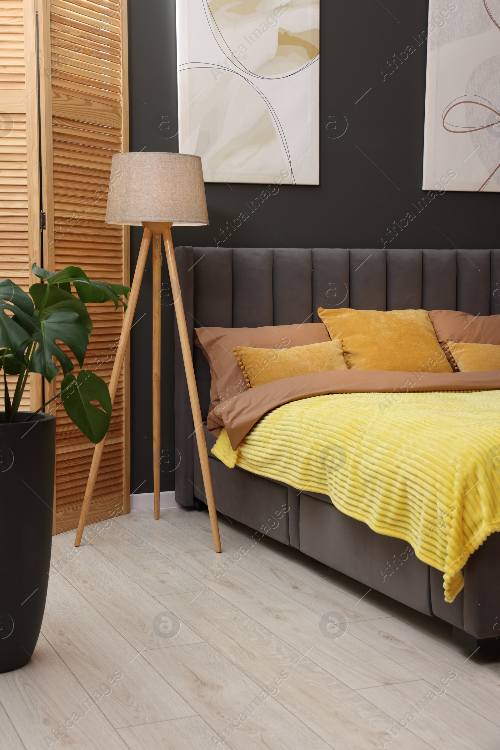Photo of Large comfortable bed, lamp and green houseplant in stylish room. Bedroom interior