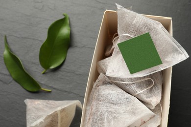 Photo of Box with paper tea bags and leaves on black table, closeup
