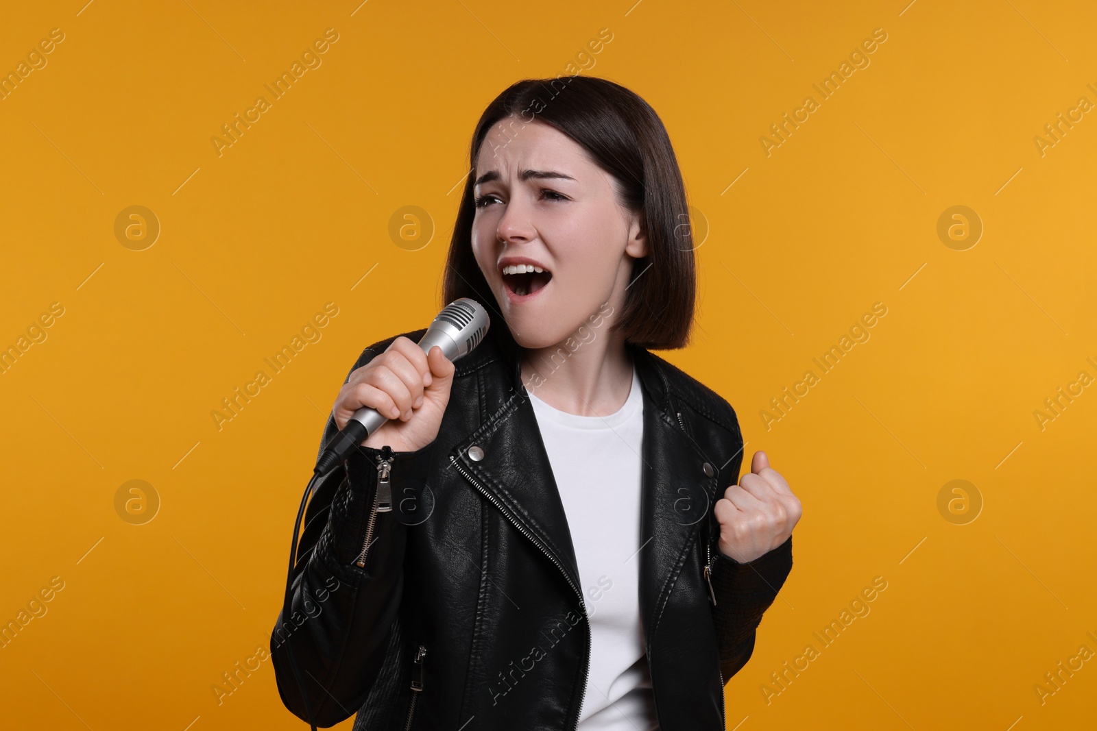 Photo of Beautiful young woman with microphone singing on yellow background