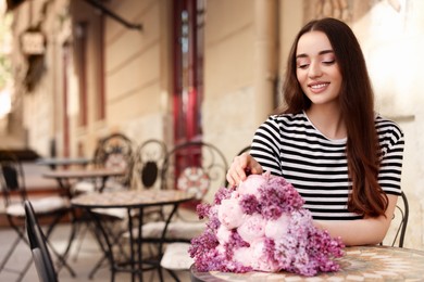 Photo of Beautiful woman with bouquet of spring flowers in outdoor cafe, space for text