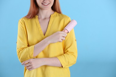 Photo of Young woman cleaning clothes with lint roller on light blue background, closeup