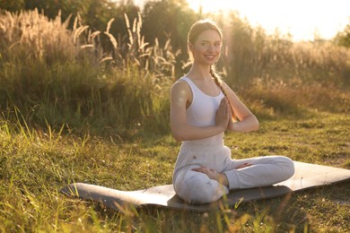 Photo of Beautiful woman practicing Padmasana on yoga mat outdoors, space for text. Lotus pose