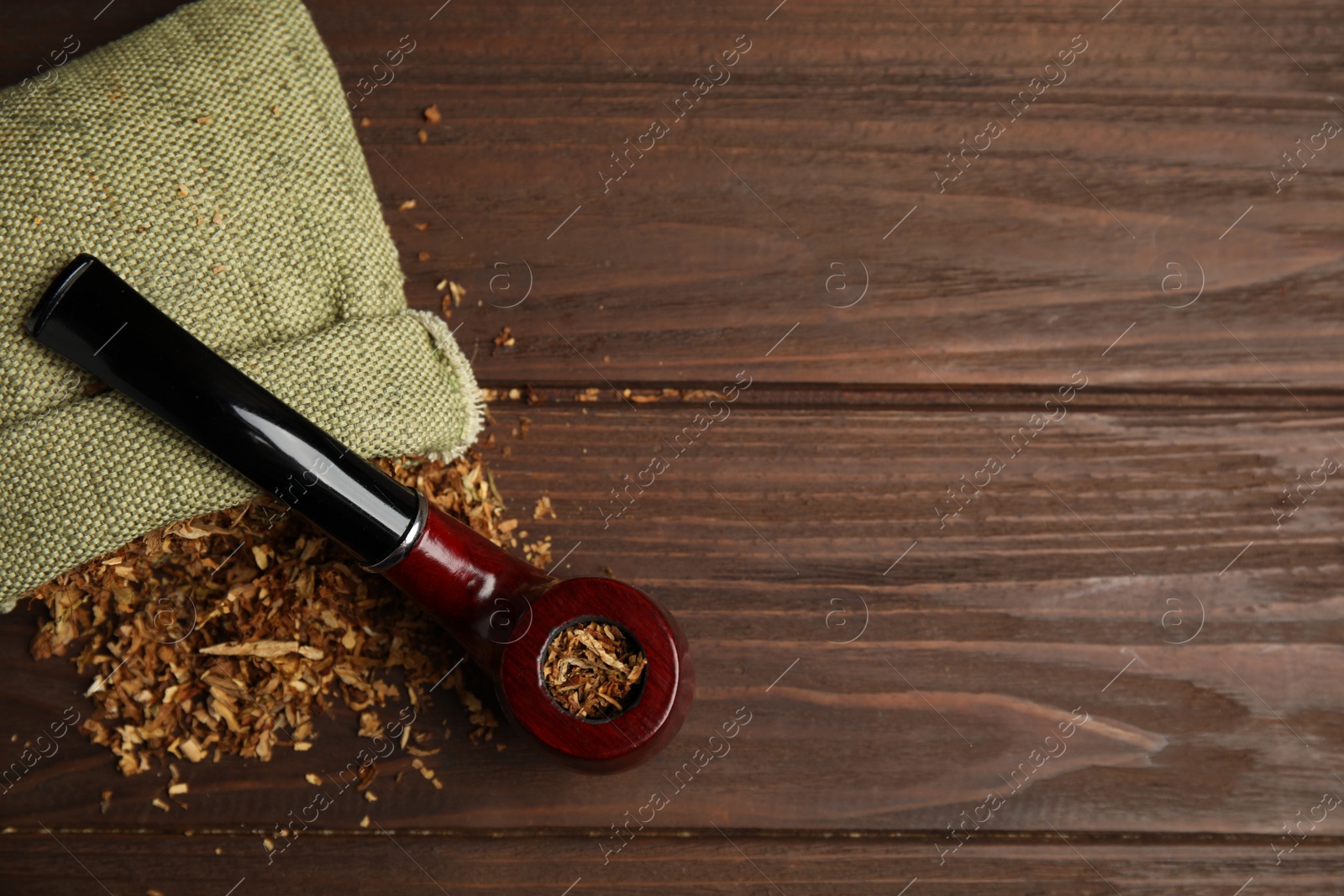 Photo of Classic smoking pipe with sack of tobacco on wooden table, flat lay. Space for text