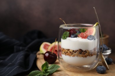 Photo of Glass with yogurt, berries, mint and granola on wooden table. Space for text