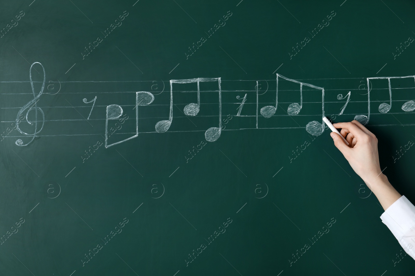 Photo of Woman writing music notes with chalk on blackboard, closeup