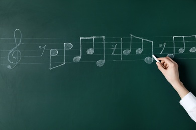 Photo of Woman writing music notes with chalk on blackboard, closeup