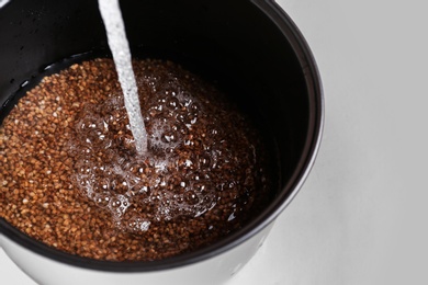 Photo of Pouring water into multi cooker with buckwheat on light background, closeup