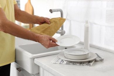 Photo of Man with towel putting plate on stack of ones in kitchen, closeup