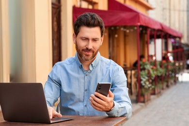 Photo of Handsome man using smartphone and laptop at table in outdoor cafe