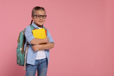 Happy schoolgirl in glasses with backpack and books on pink background, space for text