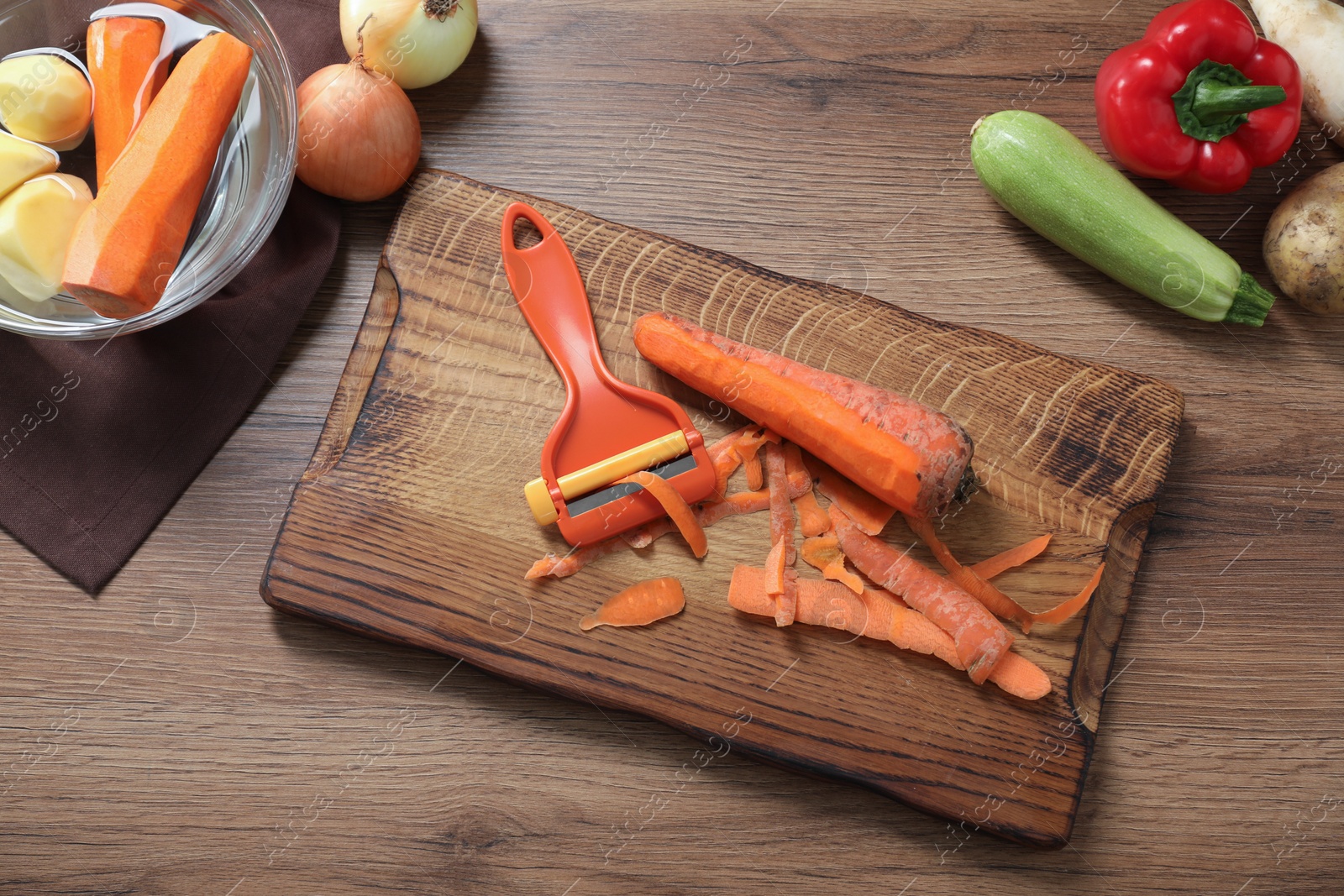 Photo of Peels, peeler and fresh vegetables on wooden table, flat lay