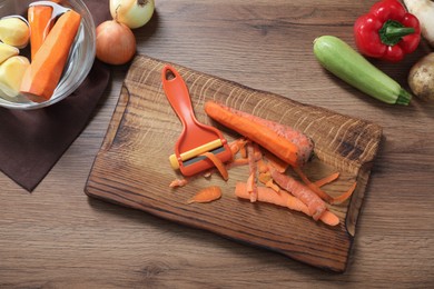 Photo of Peels, peeler and fresh vegetables on wooden table, flat lay
