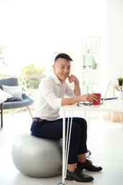 Photo of Happy young businessman sitting on fitness ball in office. Workplace exercises