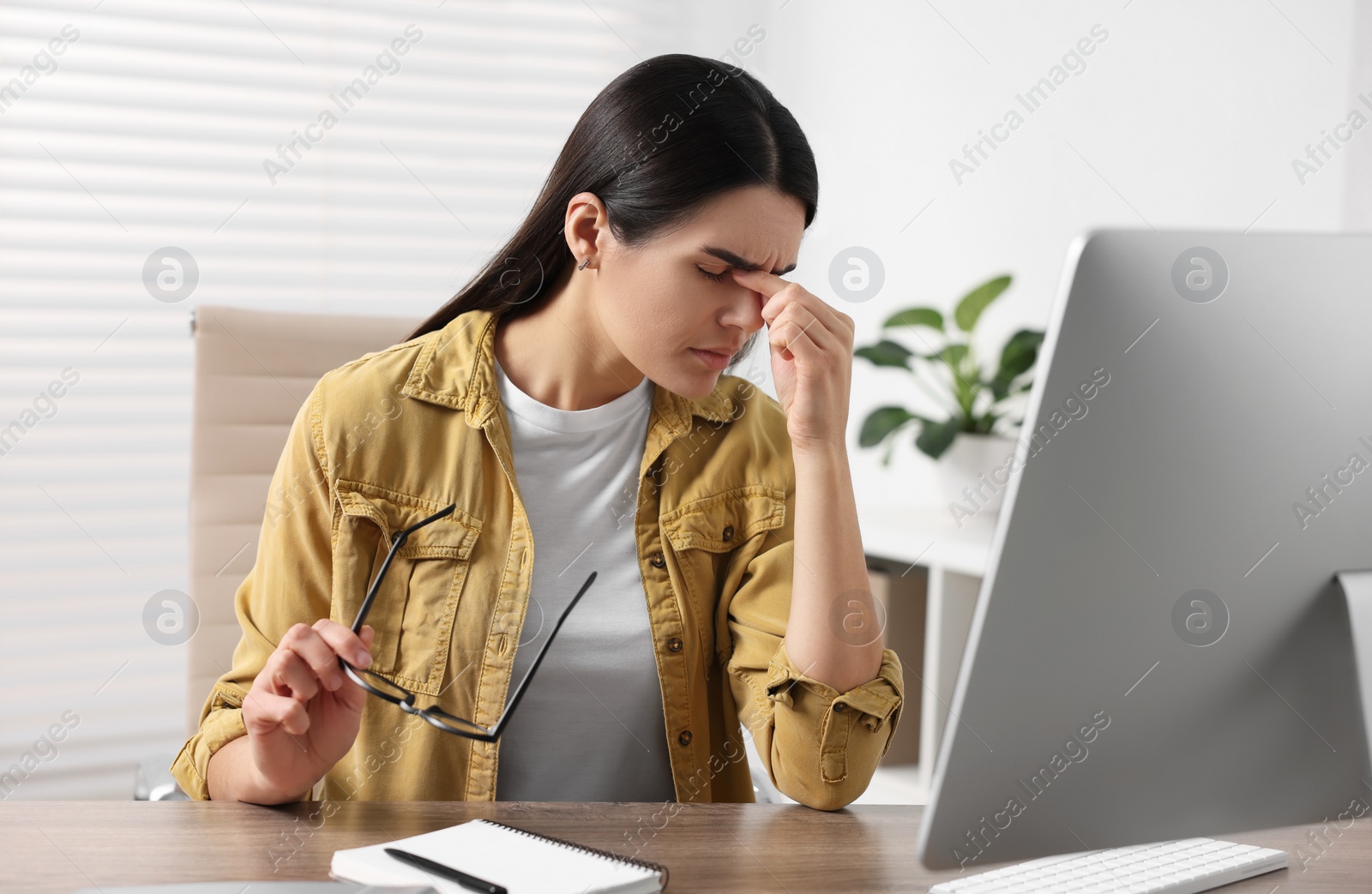 Photo of Young woman suffering from headache at wooden table in office