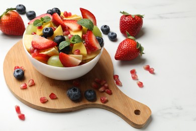 Photo of Tasty fruit salad in bowl and ingredients on white table