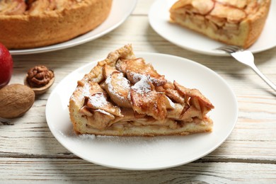 Slice of delicious apple pie with powdered sugar served on white wooden table