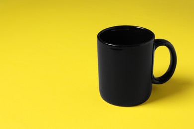 Photo of One black ceramic mug on yellow background, space for text