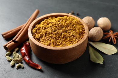 Dry curry powder in bowl and other spices on dark table, closeup