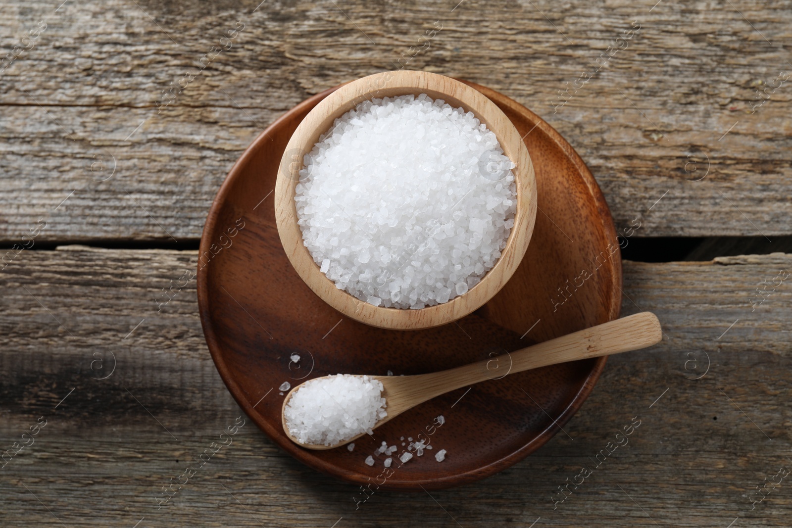 Photo of Organic salt in bowl and spoon on wooden table, top view