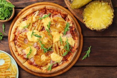 Photo of Delicious pineapple pizza and ingredients on wooden table, flat lay