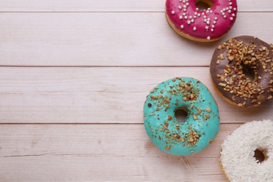Different tasty donuts on white wooden table, flat lay. Space for text