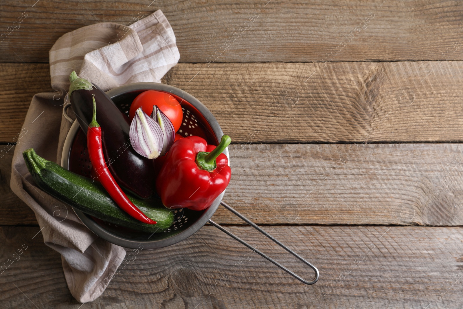 Photo of Fresh vegetables for ratatouille in colander on wooden table, flat lay. Space for text