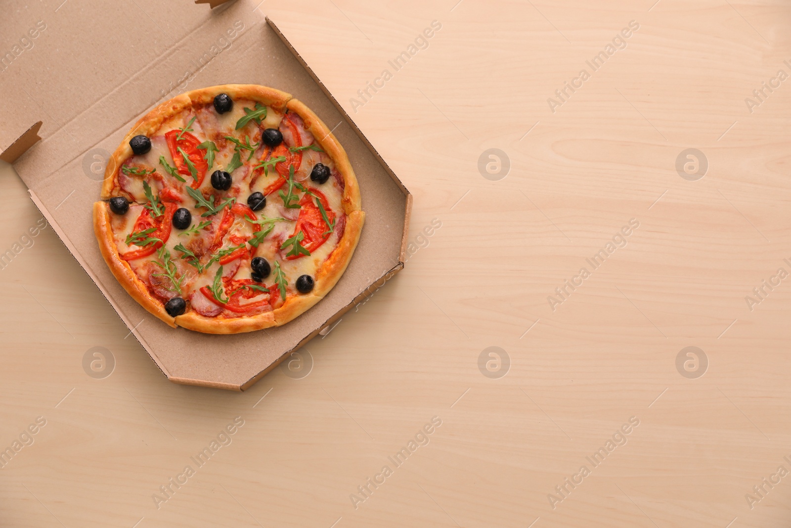 Photo of Cardboard box with tasty pizza on wooden background, top view with space for text