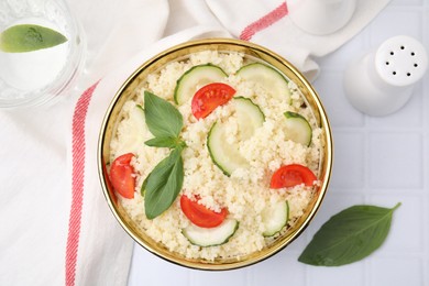 Photo of Tasty couscous with tomatoes, cucumber and basil on white tiled table, flat lay