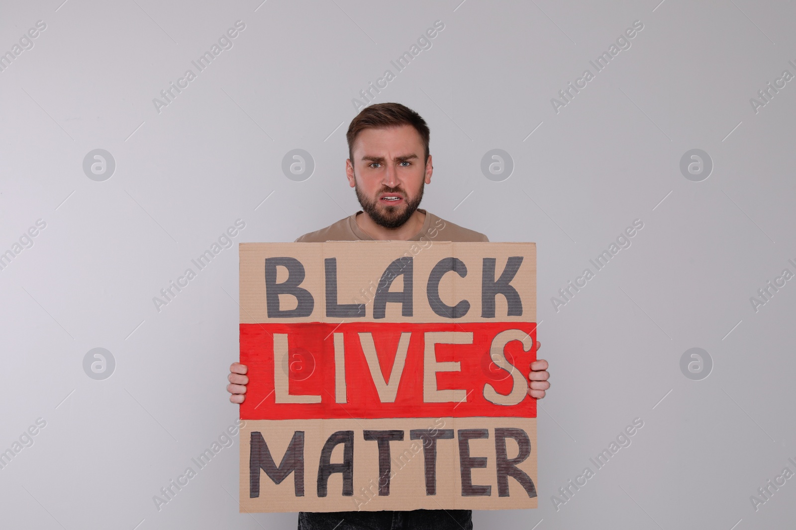 Photo of Young man holding sign with phrase Black Lives Matter on light background. End racism