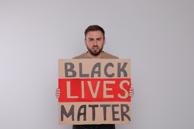 Young man holding sign with phrase Black Lives Matter on light background. End racism