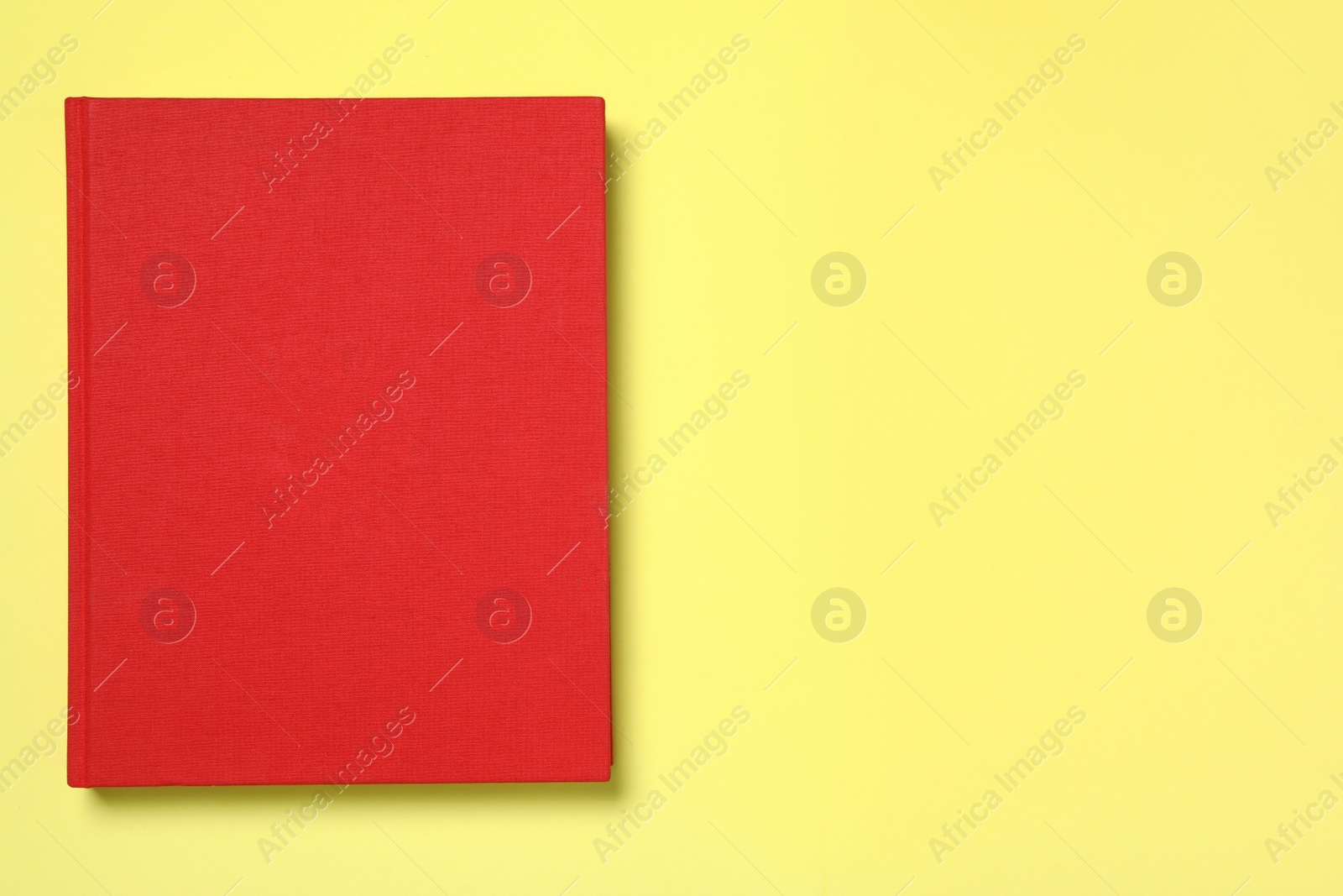 Photo of Book with red cover on yellow background, top view. Space for text