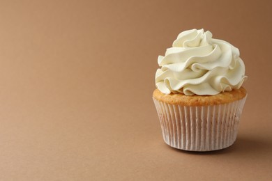 Tasty vanilla cupcake with cream on dark beige background, space for text