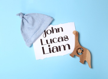 Photo of List of different baby names and child's accessories on light blue background, flat lay