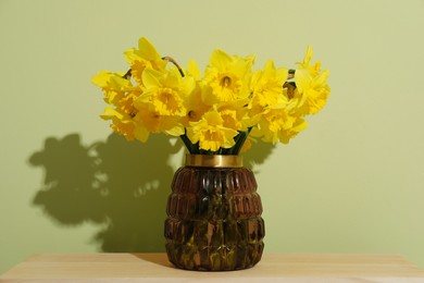 Beautiful daffodils in vase on table near light green wall