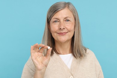 Photo of Senior woman with pill on light blue background
