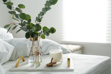 Photo of Eucalyptus branches, candle and aromatic reed air freshener on bed indoors, space for text. Interior elements